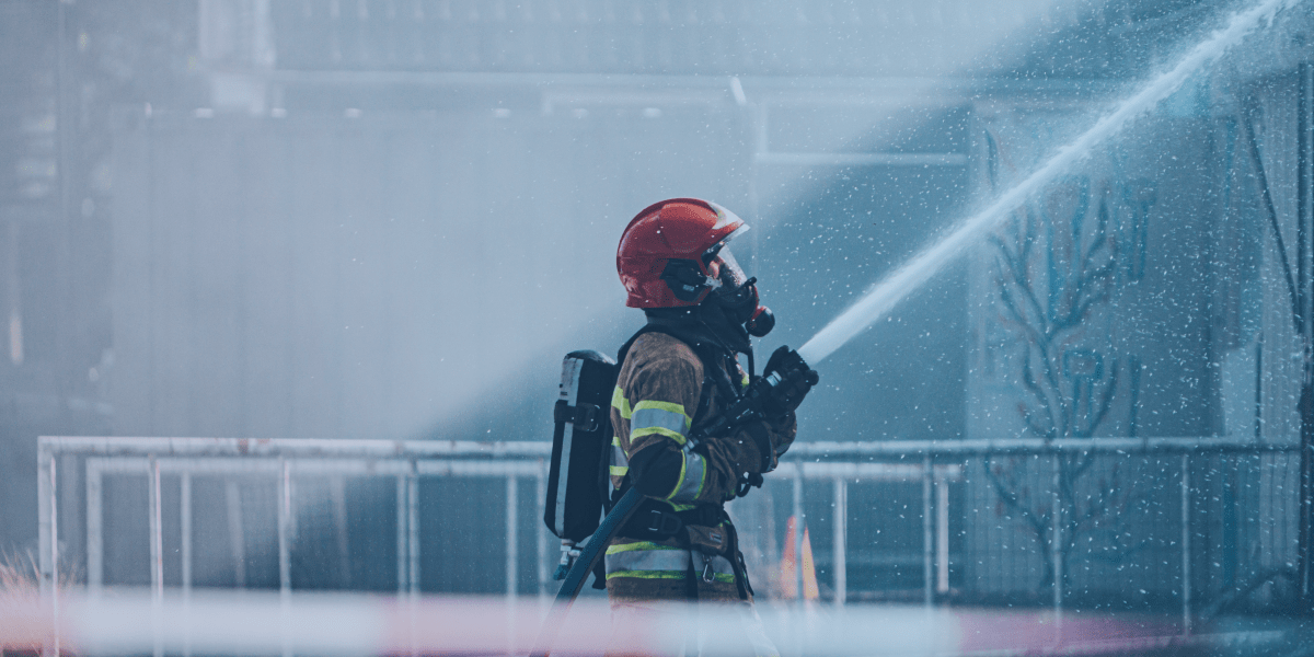 bombeiro apontando a mangueira de incêndio com o jato de água na direção de um lugar alto